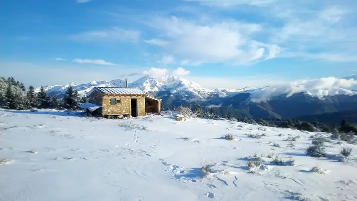 Une cabane de berger en pierre dans la neige, face aux montagnes