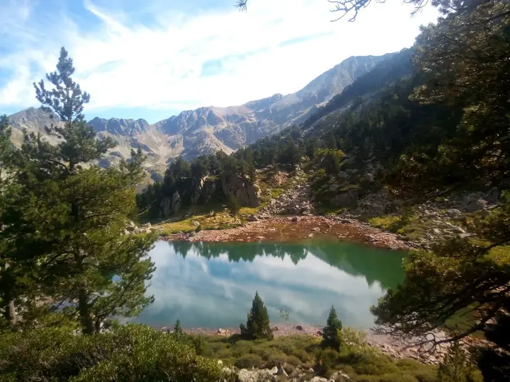 Un étang de montagne entouré de pins, avec les sommets en reflet